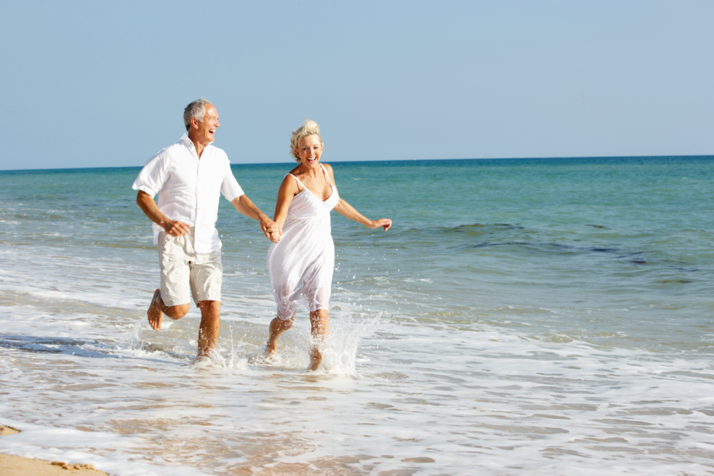 A man and woman joyfully running together along the shoreline of the ocean, with waves splashing around them.