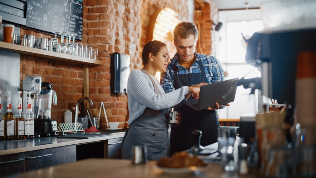 A man and woman standing in front of a bar, looking at a tablet.