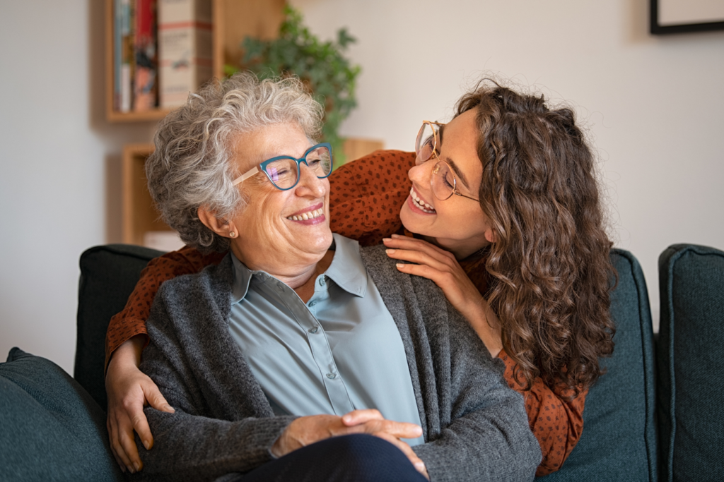 A young woman embraces an elderly woman warmly while sitting together on a sofa.