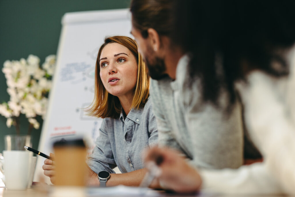 A woman discussing with two colleagues at a conference table.