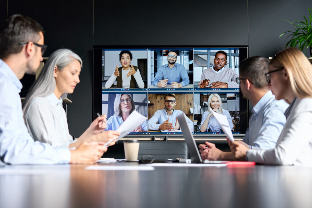 Global corporation online videoconference in a meeting room with diverse people sitting in a modern office with colleagues on a big screen