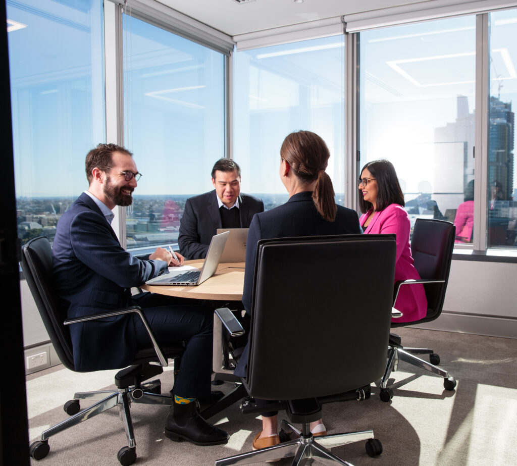 four people in meeting room at round table working and smiling